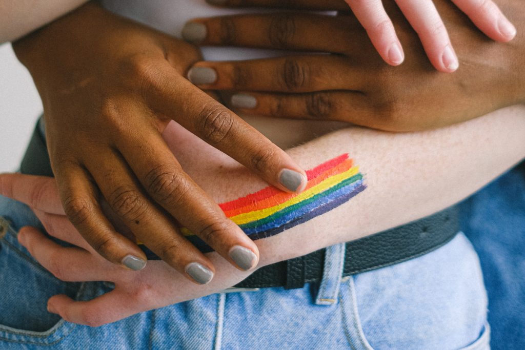 Close up of two diverse hands holding each other with a rainbow on one of the hands