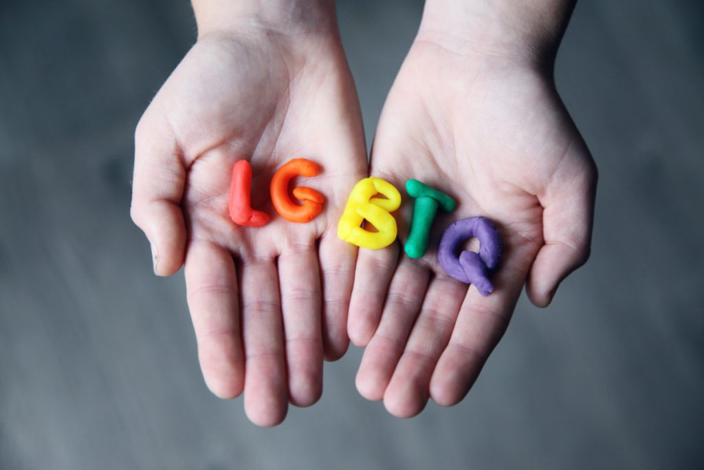 LGBTQ letters made up of rainbow coloured playdoh sitting on a pair of hands