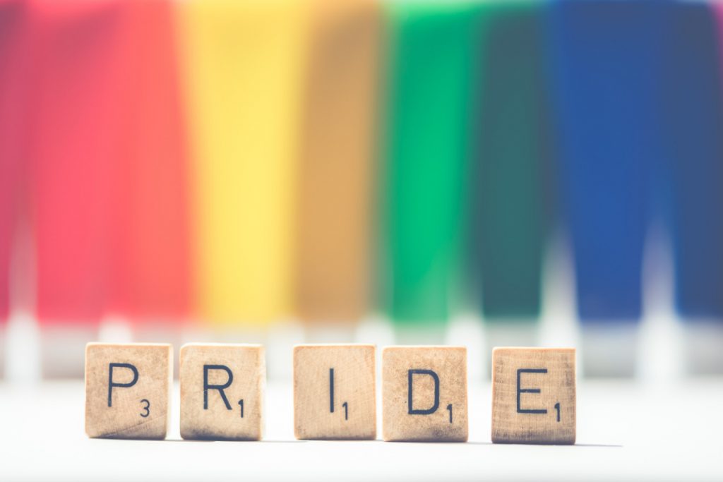 Scrabble tiles showing the words PRIDE upon a background of a rainbow