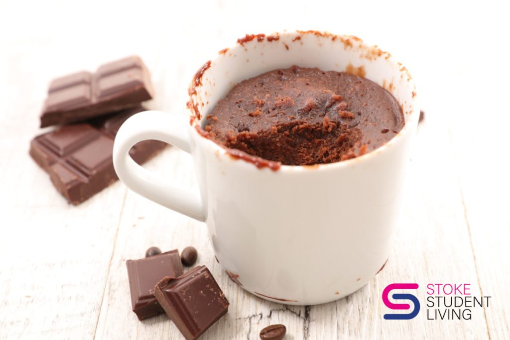 Close up of a microwave chocolate mug cake on a white background with some chunks of chocolate near by.