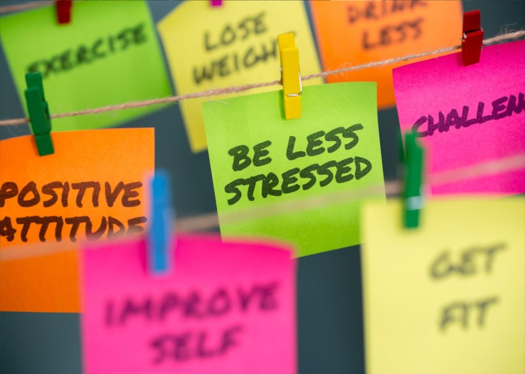 Colourful postit notes are pegged on some string saying things like 'Be less stressed', 'improve self' and 'positive attitude'.